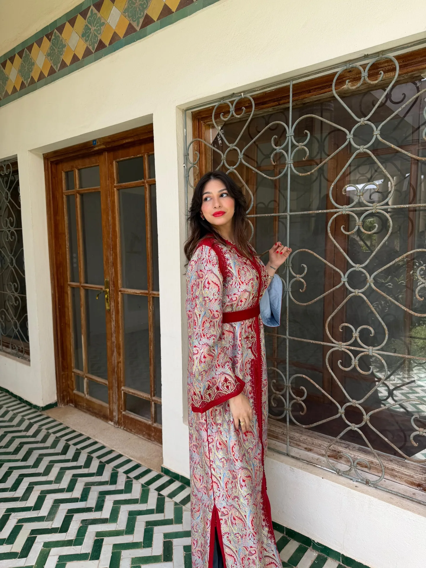 Caftan brocart grenat vu de profil devant une porte traditionnelle